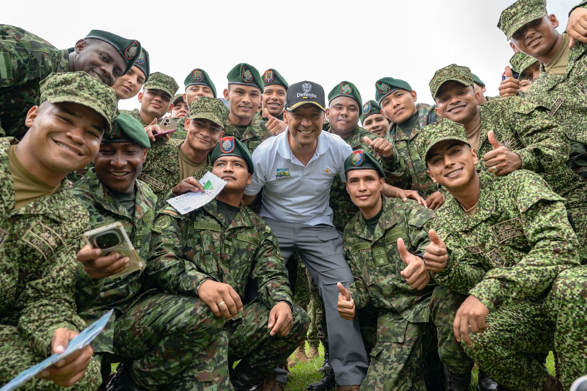 Pedro Sánchez Suárez, de civil, posa sonriente en medio de un grupo de soldados de boina verde, muchos con el pulgar arriba, en una foto grupal cercana al aire libre.