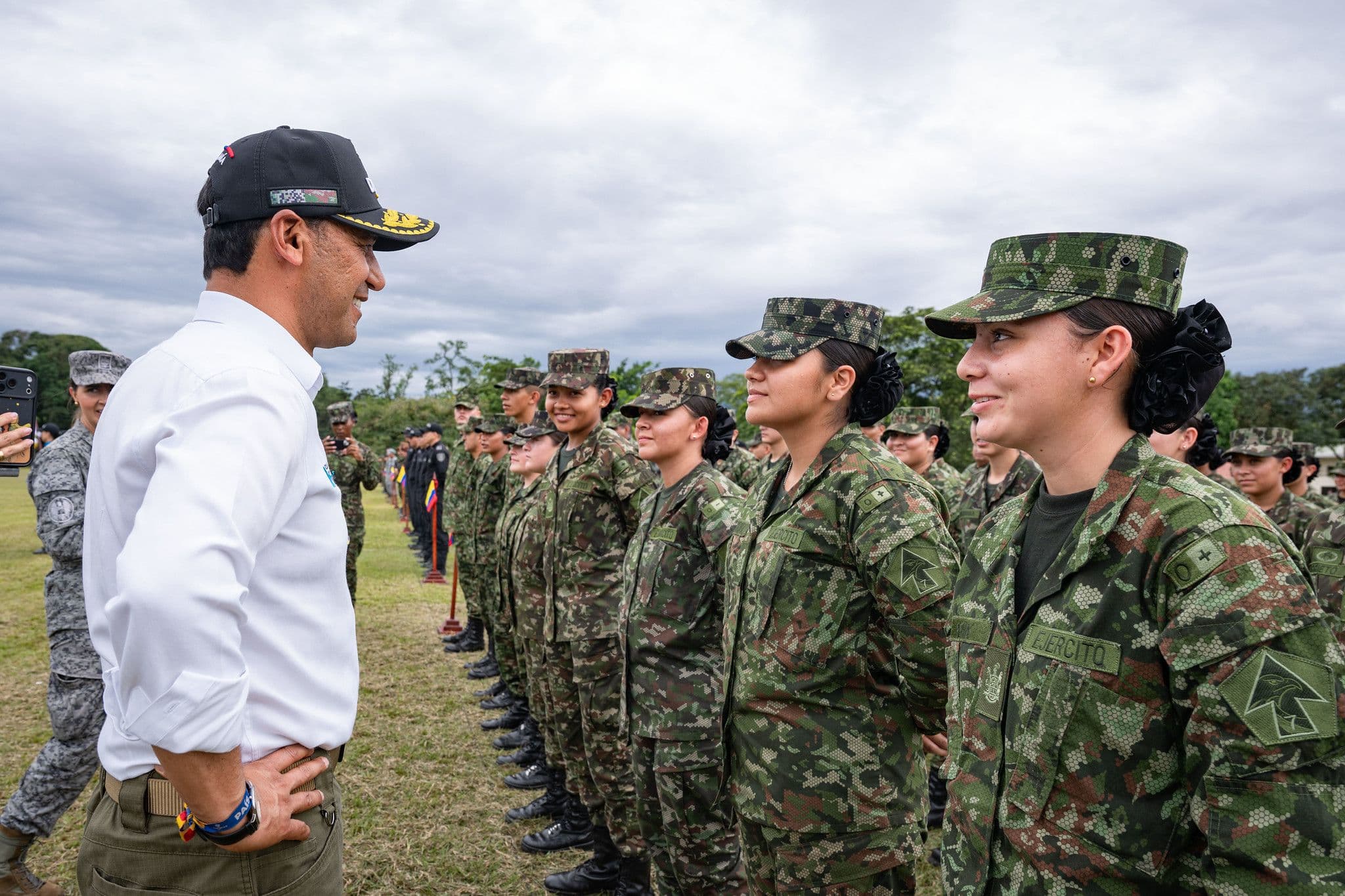 Pedro Sánchez Suárez, de civil, sonríe frente a una fila de mujeres soldado del Ejército en formación, al aire libre bajo un cielo nublado.