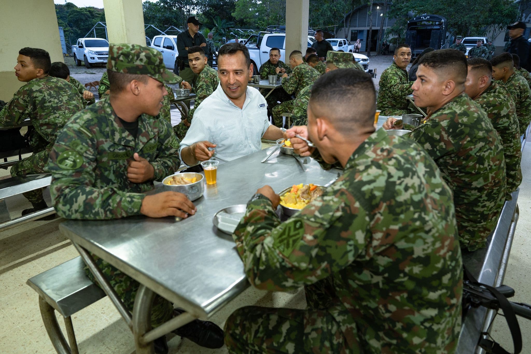 Pedro Sánchez Suárez, de civil, comparte una comida y conversa con soldados en mesas metálicas bajo un techado al aire libre, rodeado de más militares comiendo.
