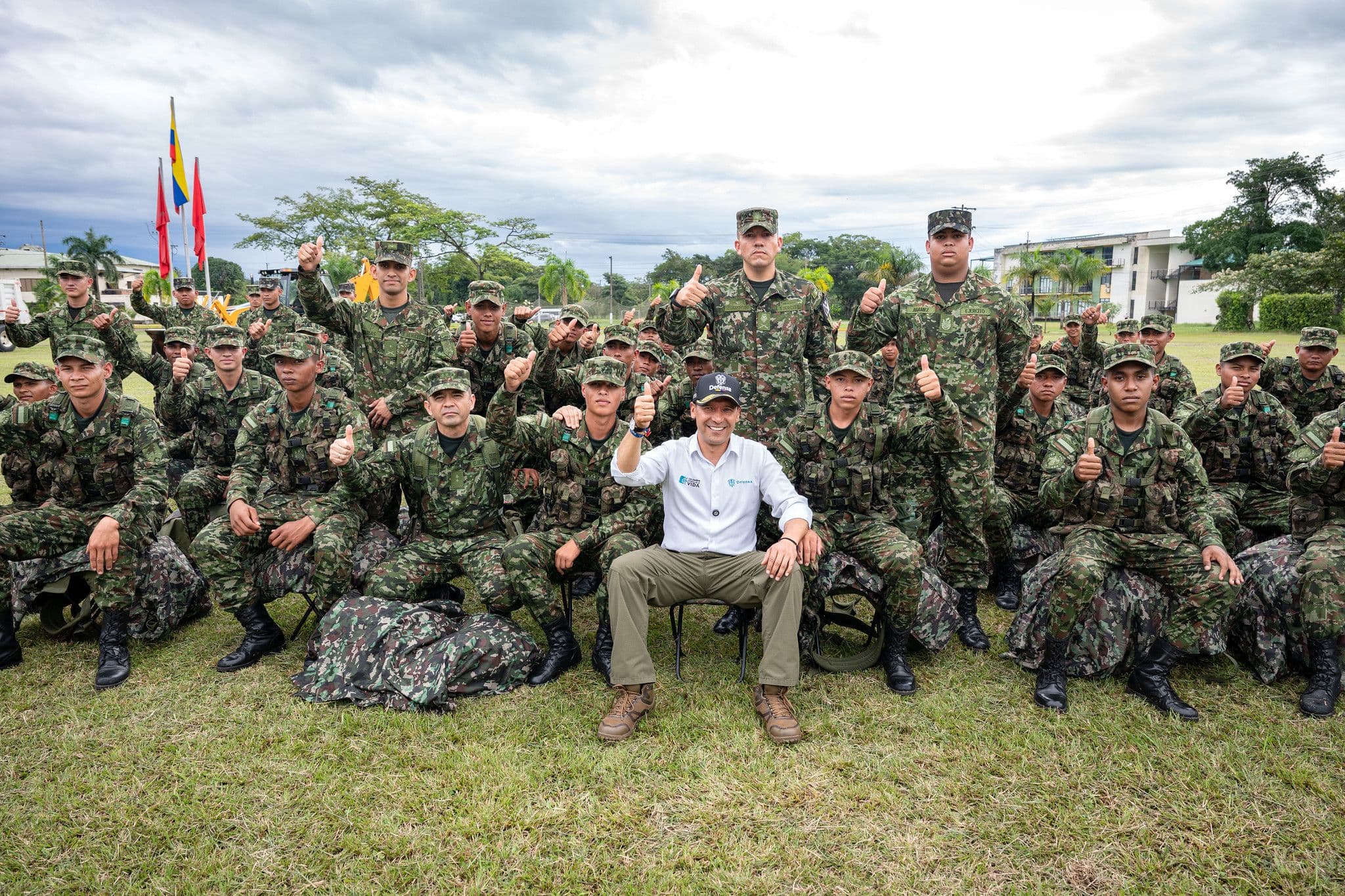 Pedro Sánchez Suárez, de civil, posa sentado en el centro de un gran grupo de soldados en uniforme de campaña, la mayoría con el pulgar arriba, en una foto grupal al aire libre sobre césped.