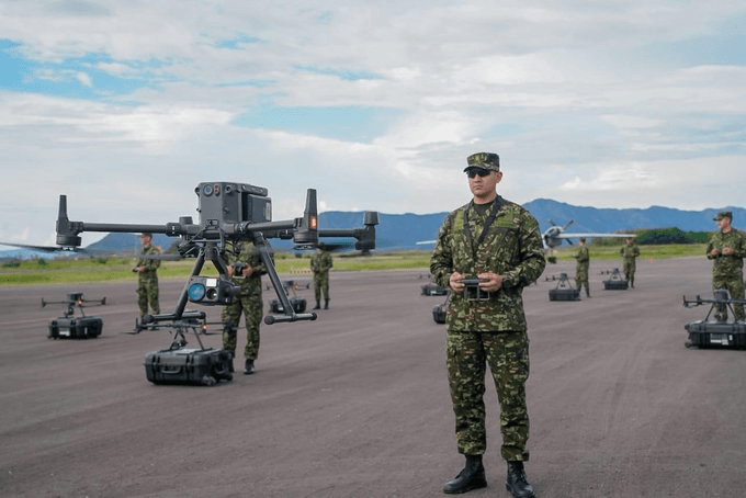 Soldados del Ejército Nacional operan drones en una pista de aterrizaje; en primer plano un uniformado sostiene un control remoto y detrás se eleva un dron multirrotor
